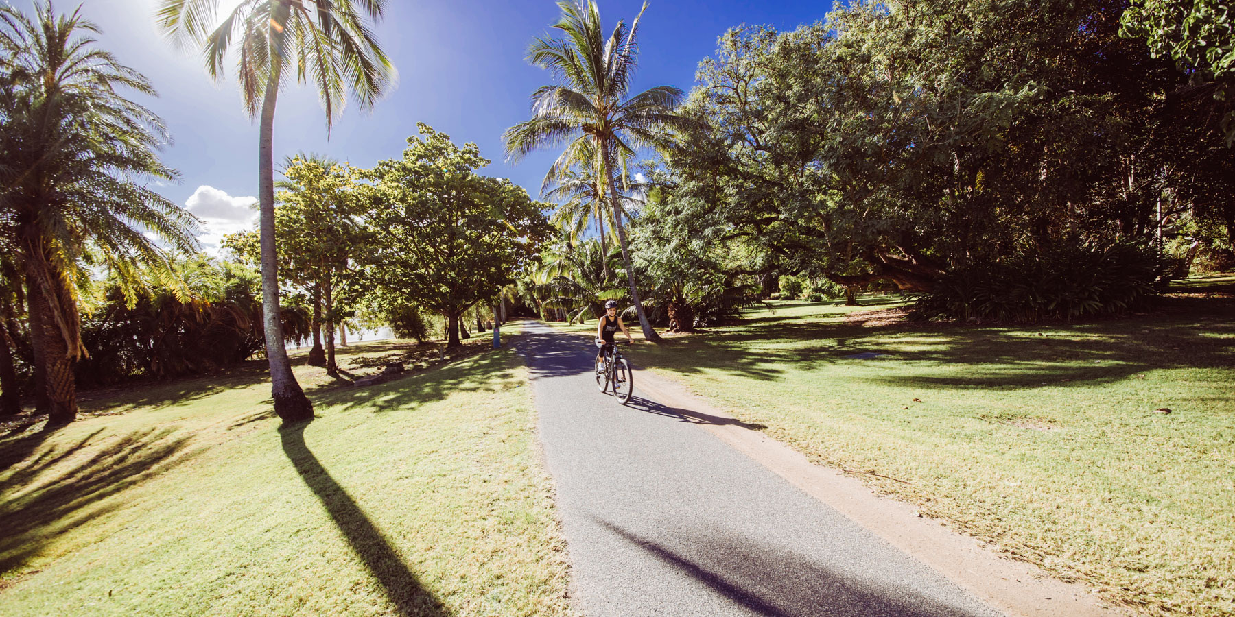 Woman riding a bike on pathway with trees on sides in Rockhampton Botanic Gardens